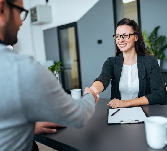 Woman shaking hands with man sitting across from her at desk