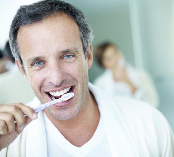 Man smiling while brushing his teeth
