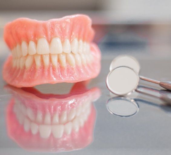 Full dentures on table next to two dental mirrors