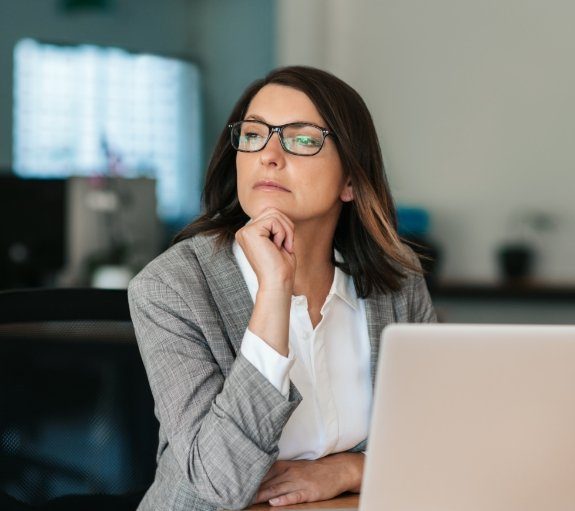 Woman sitting at desk with laptop and staring into the distance