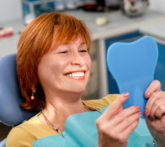 A senior woman admiring her new implant dentures in a hand mirror